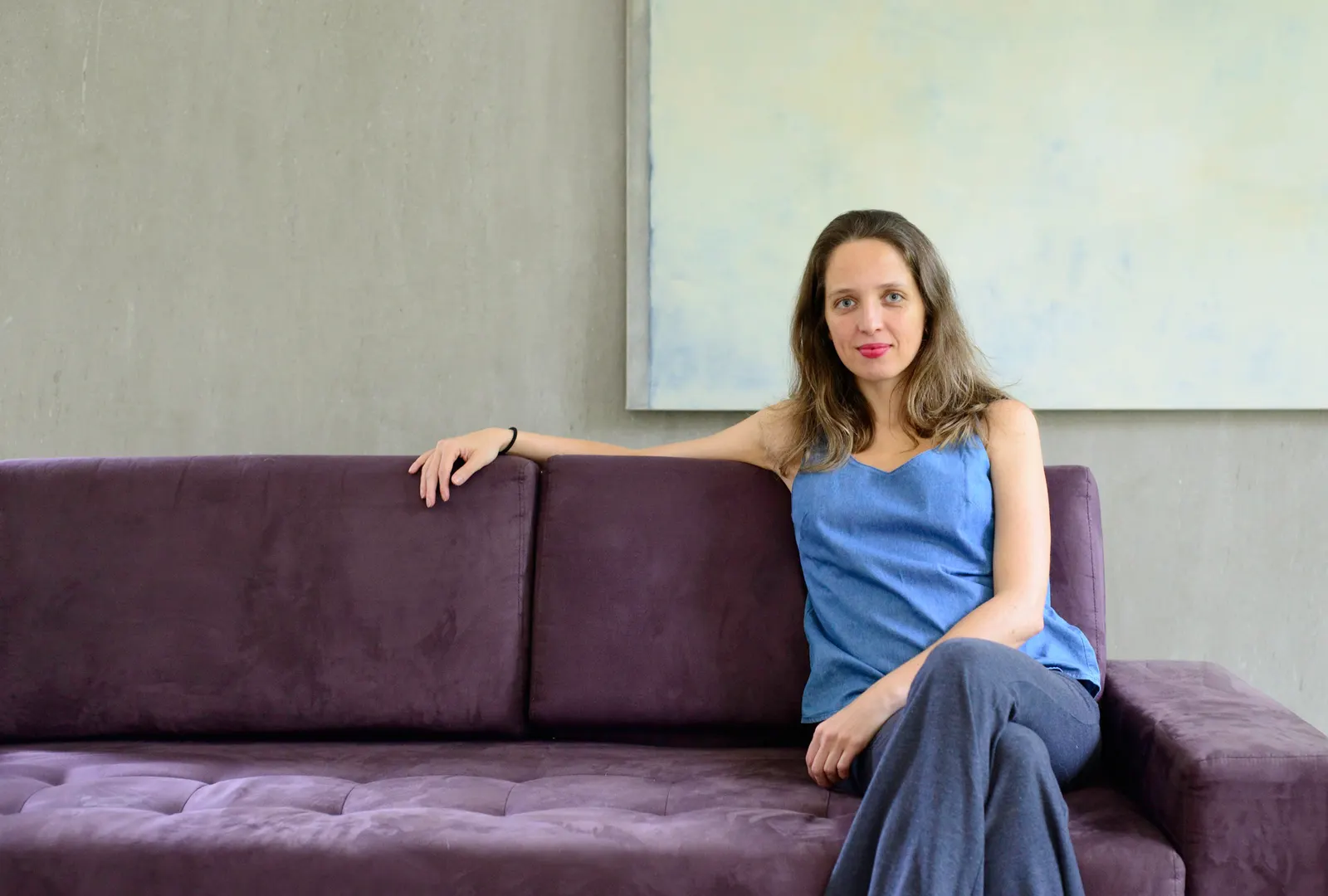 Mirella Duarte sentada em um sofá, sob uma pintura de tons claros